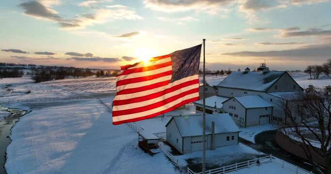American family farm with proud USA flag in winter snow. Sunrise beautiful scene. Aerial orbit.