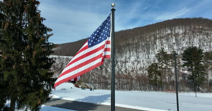 American flag waves in breeze. Winter mountain snow scene. Pine tree and forest.