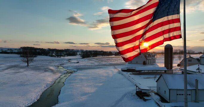 American flag waves in wind, breeze. Rural America field and stream at sunset. Agriculture theme in winter snow.