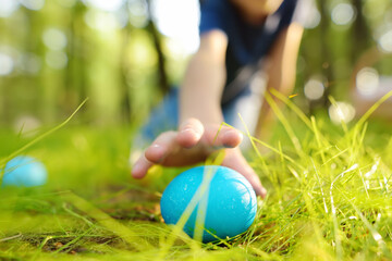 Little boy hunting for egg in spring garden on Easter day. Traditional easter festival outdoors. Focus on multicolor eggs. - 483676407