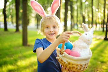 Little boy wearing bunny ears costume hunting for eggs in spring garden on Easter day. Traditional easter festival outdoors.