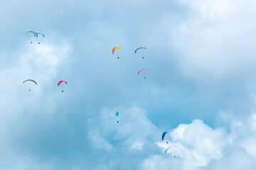 Many Paragliders of Various Colors Flying on a Blue Background full of Clouds