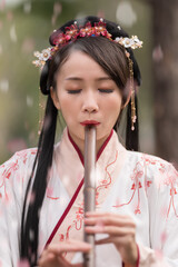 A young woman in Chinese traditional style dress playing bamboo flute with falling petals © imphilip