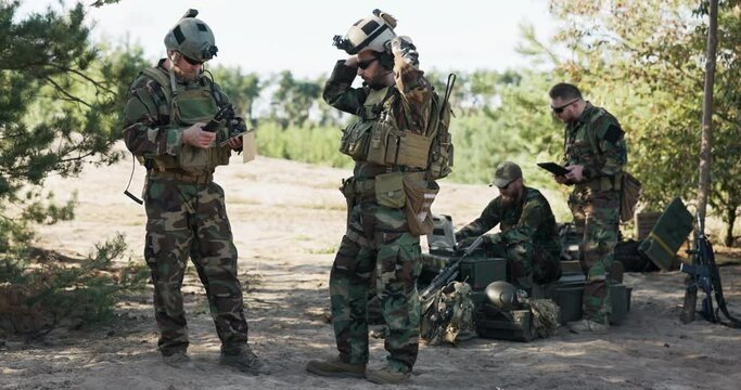 A group of soldiers is getting ready to go on a patrol in the field, they set up a strategy, a location, they follow a map on a computer, a tablet, a troop leader puts on a helmet