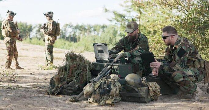 Soldiers belonging to powerful army are preparing strategy to fight surprise enemy enter data into system talk hold tablet dressed in uniforms moro, camouflage, helmets, backpacks, training ground