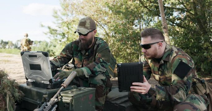 Soldiers belonging to powerful army are preparing strategy to fight surprise enemy enter data into system talk hold tablet dressed in uniforms moro, camouflage, helmets, backpacks, training ground
