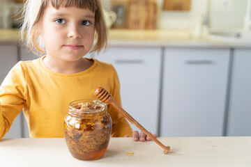 Child girl eating golden honeycomb and beeswax in a jar of honey on the table. Fresh organic honey...