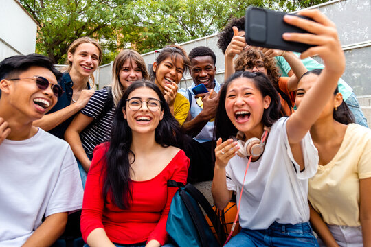 Multiracial group of teen friends take selfie laughing together outdoors.