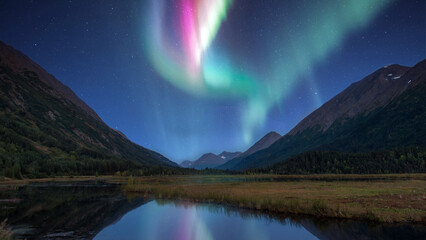 Aurora Borealis lighting up the sky over the mountains and a lake in Alaska on the Kenai Peninsula