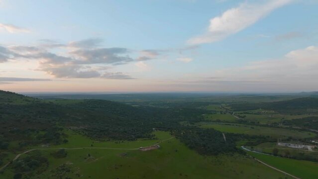 Beautiful sunset colors over the horizon on the green stretched landscape near Alconchel in the province Extremadura in Spain on a partly cloudy day. Drone dolly shot