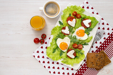 Breakfast on Valentines Day breakfast for two with heart-shaped eggs vegetables and cheese with coffee and juice on a white wooden table covered with a beautiful napkin. Healthy breakfast. Top view