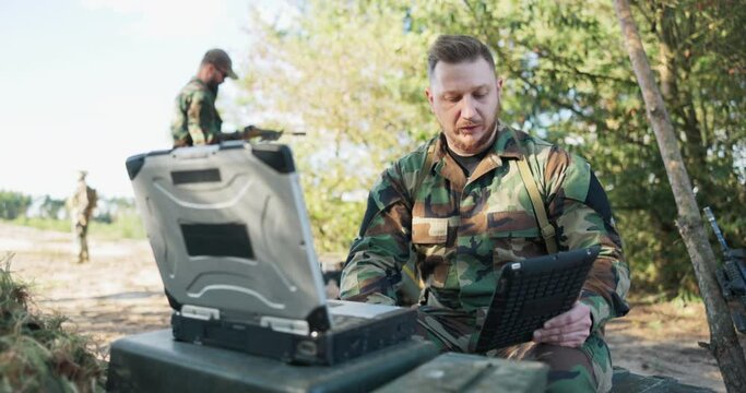 Serious experienced army commander is in field having video conversation on computer with head of army base, giving him details of action discussing precautions taken, secret information