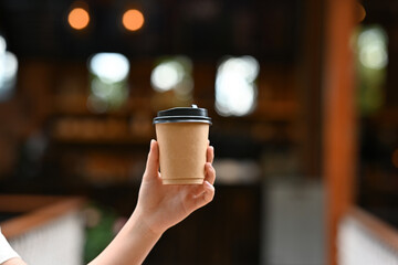 Close up with young female teenager holding a cup of take away coffee with coffee shop on the background.
