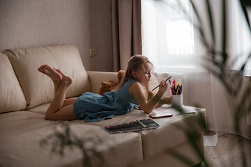 Obraz premium girl lies on the sofa in the living room and draws
