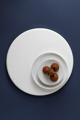Ceramic plate with sweets truffles on white round podium on blue background. Top view. Simple and minimalism.