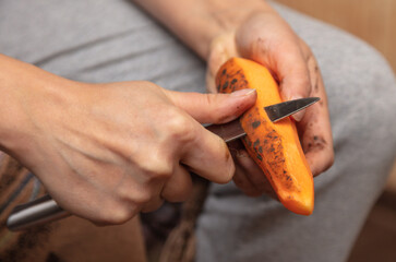 A woman peels a carrot with a knife.