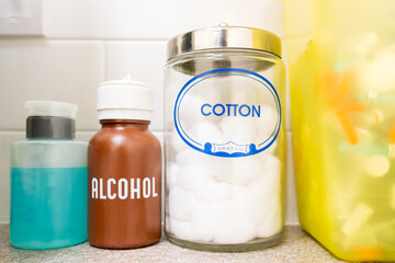 Doctor’s office typical sanitation supplies on counter, close up of rubbing alcohol, cotton balls and syringe safe medical waste basket.