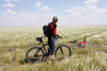 Obraz premium Smiling man with his bicycle stands in the steppe, overgrown with feather grass. Active leisure concept.