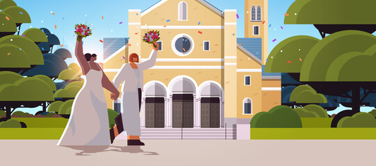 newlywed lesbian couple with flowers standing near church transgender love LGBT community wedding celebration