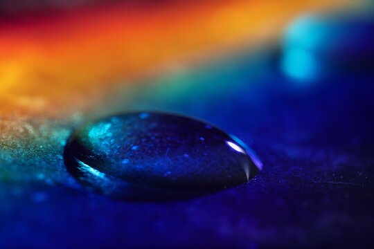 Raindrop on green leaf in rays of rainbow. Beauty of natural color in drop of ultra-macro. Bright colors excite delight