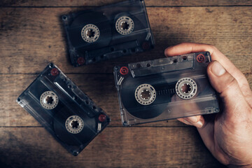 Hand holding audio cassette tape on brown old wooden table. Minimalism retro style concept....