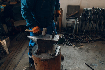 Blacksmith forges and making arrow arrowhead metal detail with hammer and anvil at forge.