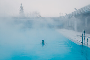 Fit swimmer male training swim in open winter swimming pool with fog. Geothermal outdoor spa health concept.