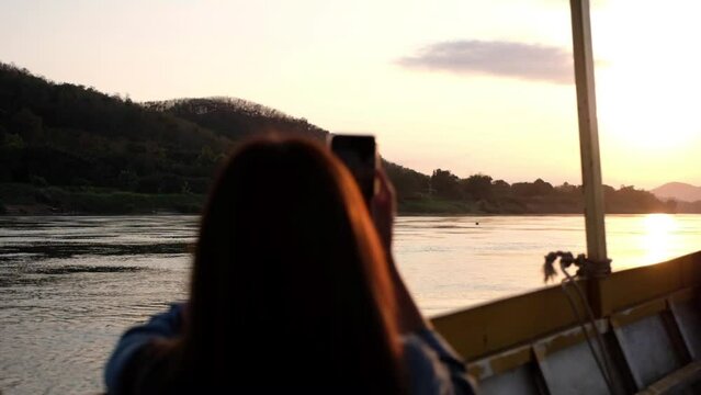 Slow motion of a female traveler taking photo while sailing long tail boat in the Mekong river before sunset