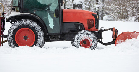 Tractor cleaning urban park paths on a cold snowy day.