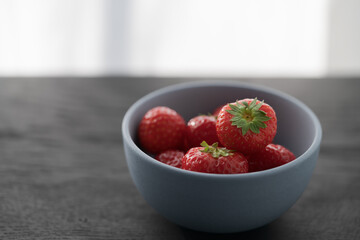 Organic ripe strawberries in blue ceramic bowl on black oak table