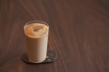 Ice coffee wih milk in tumbler glass on black walnut table