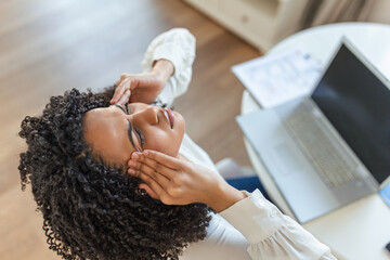 Exhausted businesswoman having a headache in home office. African American creative woman working at office desk feeling tired. Stressed business woman feeling eye pain while overworking