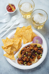 Nachos chips with minced meat and beans served on a takeaway plate, elevated view on a light-blue stone surface, vertical shot