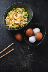 Bowl of chinese traditional egg fried rice, vertical shot on a dark-brown stone background, high angle view, copyspace