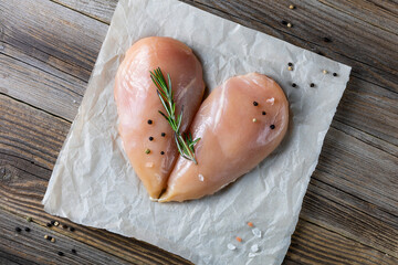 Raw chicken fillet in the shape of a heart with rosemary and spices on natural wooden background.