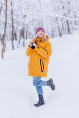 Fototapeta na wymiar Happy girl photographer in a yellow jacket takes pictures of winter in a snowy park
