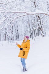 Fototapeta na wymiar Happy girl photographer in a yellow jacket takes pictures of winter in a snowy park