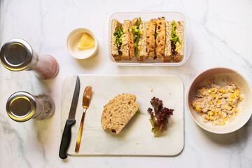 Preparing healthy sandwiches; super grains sliced bread, tuna, corn, avocado, lemon and vegetables on marble cutting board. Top view