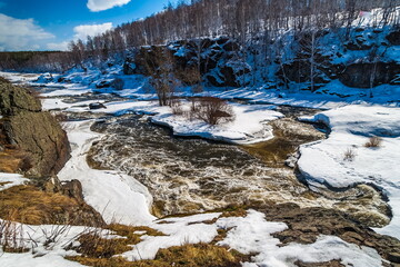 Spring landscape with river, rocks, ice, snow, trees and blue sky with white clouds