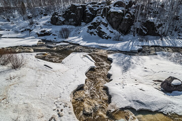 Fast river, rocks, ice, snow, trees, shrubs, dry grass in spring