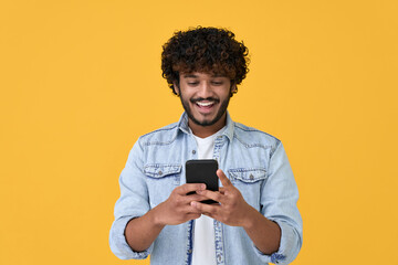 Happy indian young man using cell phone isolated on yellow background. Smiling ethnic hipster guy...