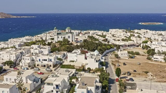 Naousa Paros Greece Aerial v2 low flyover small village capturing faneromeni church surrounded by beautiful coastal whitewashed buildings with paros park hilltop in the background - September 2021