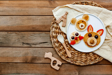 Pancakes With Funny Faces Decorated For Kids. Healthy Fruit Pancakes For baby Meal over wooden background, top view
