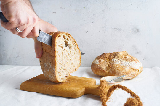 Cutting a loaf of sourdough bread on a white linen background