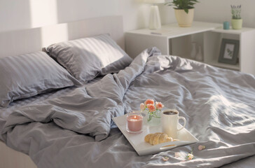 Fototapeta na wymiar cup of coffee with croissant and pink roses on bed in bedroom