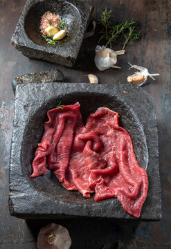 Raw beef fillet on black stone plate and mortar with herbs. Black background