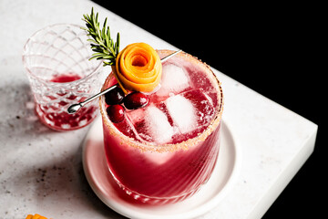 Cranberry orange margarita  on the edge of a counter with an orange peel rose and sprig of rosemary.