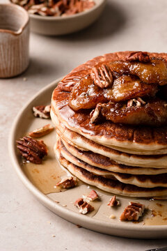 A plate of maple pecan pancakes with caramelized bananas on a table with a platter of pancakes and syrup in the background.