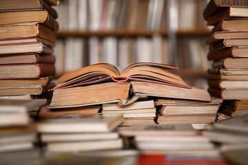 Fototapeta premium Old books on the table in the antiquarian bookshop - opened books, book pages, blurred bookshelf in the background