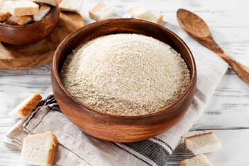 Breadcrumbs in wooden bowl on white wooden background.
